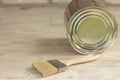 A paint brush is next to a metal can on an old white vintage wooden plank table. Brick wall in the background. Place for text or