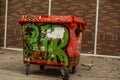 Paint brushed trash bin with graffiti against stone brick wall