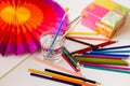 Paint brushes in glass full of water, with colour pencils, paper pad, box and rainbow coloured paper fan