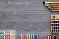 Paint brushes, paintbox with watercolors, crayons, pencils on grey wooden background, art table. Top view with copy space