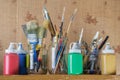 Paint brushes, painters knifes and art equipment in the glass jars with acrylic paints in the containers