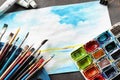 Paint brushes with watercolors and beautiful picture on table