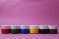 Paint in jars with white lids stands in a row, tower on a pink background: acrylic, watercolor, oil, red, yellow, blue Royalty Free Stock Photo