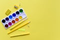 Paint, pencils and scissors. School accessories on a yellow background. View from above