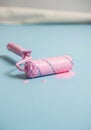 A paint roller covered in pink paint lies on a smooth, light blue surface. The roller has a Royalty Free Stock Photo