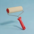 Simple beige paint roller with red handle isolated against a solid light blue background for renovation projects Royalty Free Stock Photo