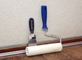 Paint roller and trowel stands in a room at baseboard near wall