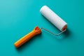 Paint roller with a white foam cover and bright orange handle placed on vibrant turquoise background for home improvement projects Royalty Free Stock Photo