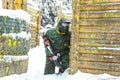 Paintball player with marker sitting on snow near wooden fortification