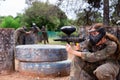 Paintball players of one team in camouflages and masks aiming with gun in shootout playing