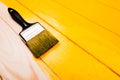 Paintbrush with black handle on yellow half freshly painted wooden background.