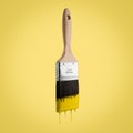 Paintbrush loaded with yellow color dripping off the bristle.