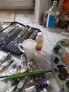 Paintbrushes, artist palette, pencils, coffee cup, watercolor and oil paints on desk in painter studio.
