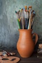 Paintbrushes in a jug from potters clay, palette and paint tubes