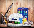 Paintbrushes, watercolor, gouache and paper are on wooden shelf