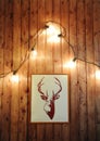 Painted deer on a wooden wall with retro garland of glowing bulbs