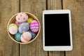 Painted Easter eggs in a bowl and digital tablet on wooden surface