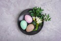 Painted Easter eggs and freesia white flower on black plate on gray textured background. Holiday table setting. Top view Royalty Free Stock Photo