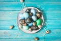 Painted eggs on plate, quail and chicken eggs, paint and brush on blue background, Easter decorations.