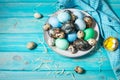 Painted eggs on plate, quail and chicken eggs, paint and brush on blue background, Easter decorations.