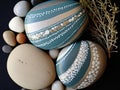 A painted flat pebble with abstract wave patterns and dots on top of a pile of stones.