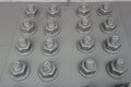 Painted gray bolts with thread with screwed nuts on the metal panel Royalty Free Stock Photo
