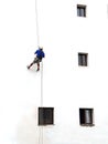 Painter of building facades. Vertical works. Worker hanging on a rope to paint white wall with roller. The vertical worker is Royalty Free Stock Photo