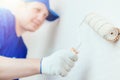 A painter in a cap and gloves paints the wall with a paint roller. Portrait of a young worker in uniform. Royalty Free Stock Photo