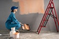 A painter in a cap is squatting near a wall, ready to paint the walls with a paint roller. Home renovation and Royalty Free Stock Photo