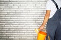 painter in coveralls holding paint brush and a bucket standing against brick wall at apartment. Royalty Free Stock Photo