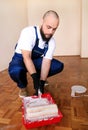 Painter with gloves holds white roller brush in his hand and mixes paint in container and red bowl for color mixing. Royalty Free Stock Photo