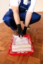 Painter with gloves holds white roller brush in his hand and mixes paint in container and red bowl for color mixing. Royalty Free Stock Photo