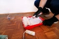 Painter with gloves holds white roller brush in his hand and mixes paint in container and red bowl for color mixing. Royalty Free Stock Photo