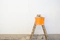 Painter ladder and bucket in front of an empty exterior wall.