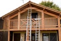 Painter ladder painting the wooden beams and railings of the house