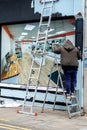 Painter Painting The Outside Of A Shop Front Standing On A Step Ladder