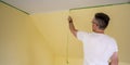 Painter removes masking tape and creates a sharp border between a yellow and white painted part of a wall