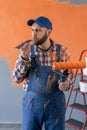 Painter with roller renovates wall. Smartphone aids painter in renovation.