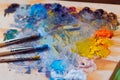 Painter`s brushes, stained with different paints, lie on wooden palette with a mess of freshly mixed bright oil paints Royalty Free Stock Photo