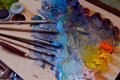 Painter`s brushes, stained with different paints, and a paletteknife lie on wooden palette with a mess of mixed bright oil paints Royalty Free Stock Photo