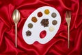 painter\'s palette full of colorful spices and golden cutlery on red satin background Royalty Free Stock Photo