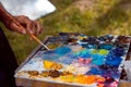 Painter`s skilful hand mixes oil paints with a brush on wooden palette, stained with a fresh stained colorful mess