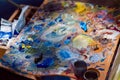 Painter`s wooden palette covered with a mess of fresh mixed bright oil paints, creative artistic disorder at summer plainair Royalty Free Stock Photo