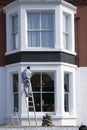 Painter on top of ladder painting white the facade of Pearl Hotel in Peterborough with perspective from down up.