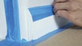 Painter Using Masking Blue Tape to Secure Baseboard, Moulding. Preparation For Room Painting