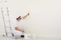 A painter in white uniform points to a white background for painting in the room.