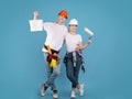 Painters couple standing with paint bucket and roller brush on blue background