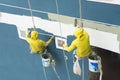 Painters hanging on roll, painting colour on building wall.