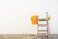 Painting accessories on a ladder in front of an empty exterior house wall.