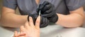 Painting female nails. Hands of manicurist in black gloves is applying transparent nail polish on female nails in a Royalty Free Stock Photo